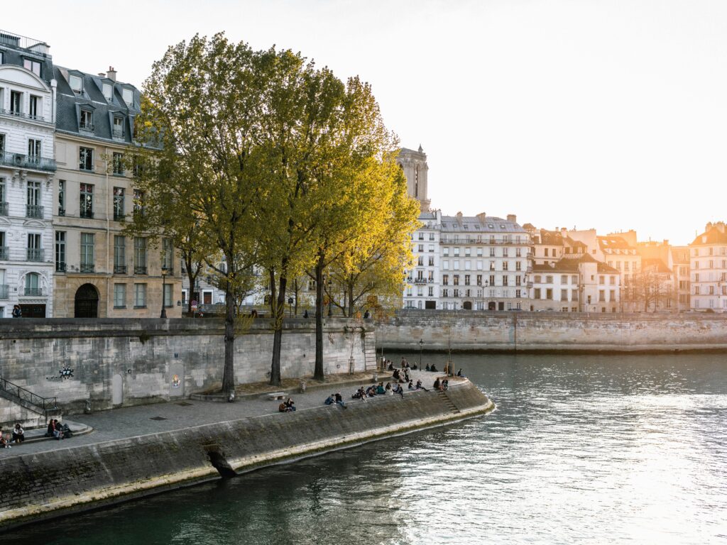 pexels-photo-2239471-2239471 View of people relaxing by the Seine River with Parisian architecture and trees in sunlight.