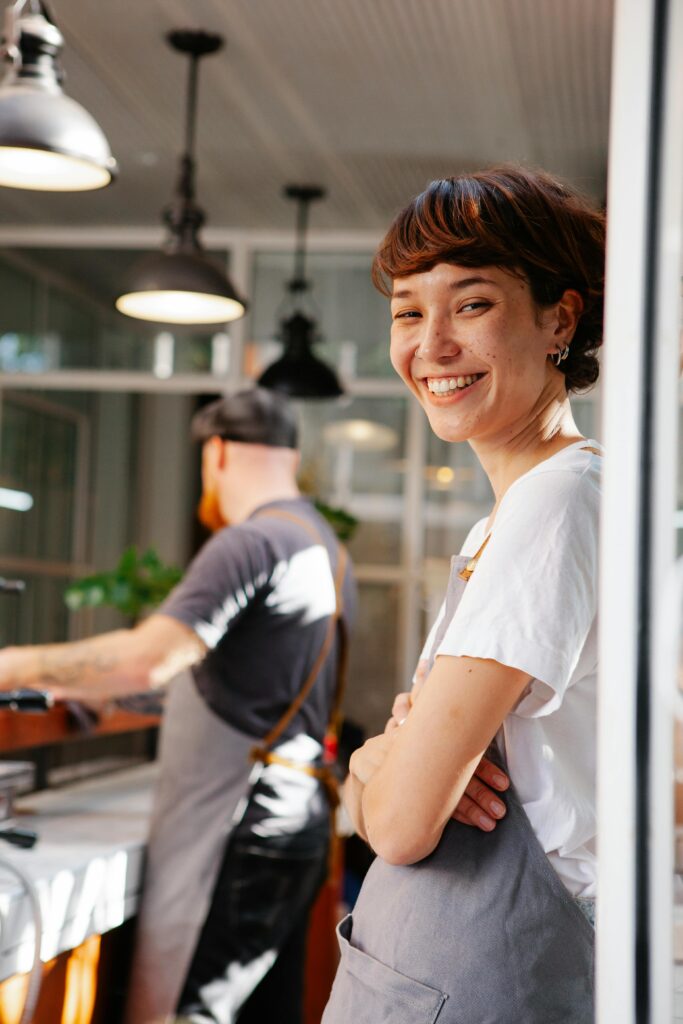pexels-photo-6205607-6205607 A cheerful barista smiling brightly in a modern cafe setting, creating a welcoming atmosphere.